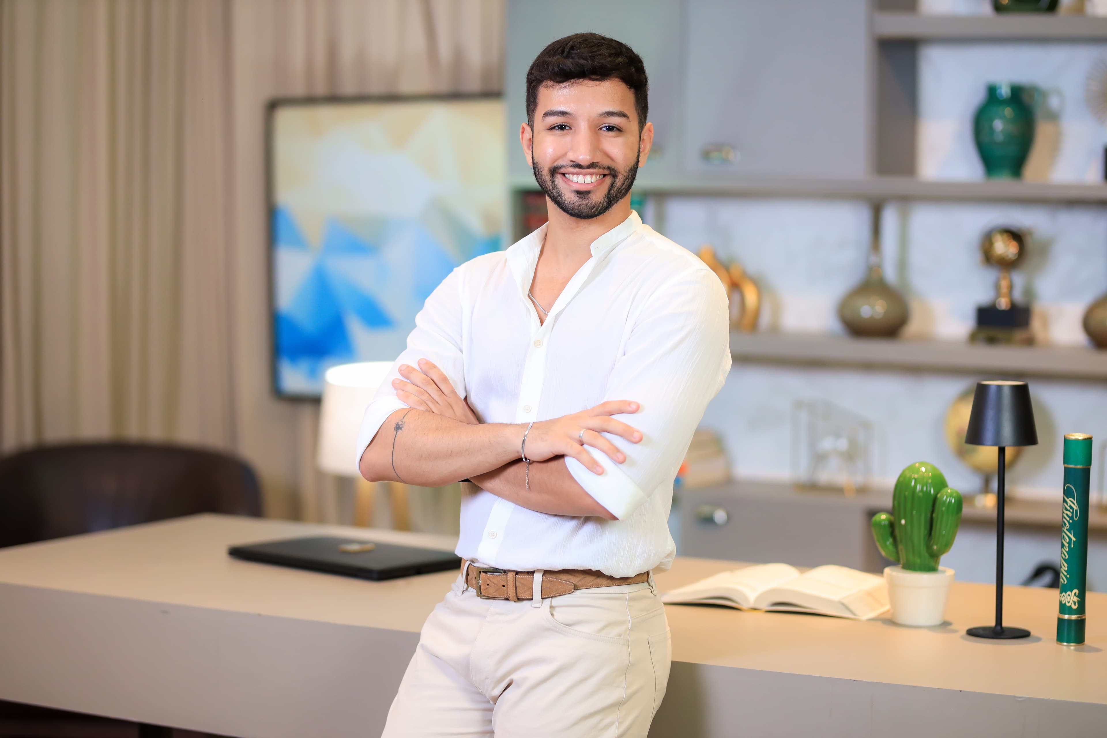 Dr. José Fernandes de braços cruzados, apoiado em uma mesa de escritório, vestindo camisa branca